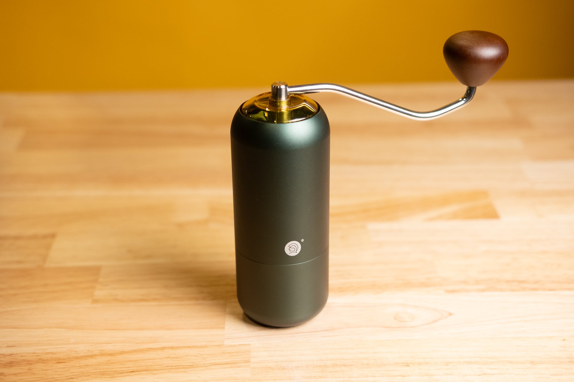 Matte dark green LAMOSE zeroHero Z7 manual coffee grinder, metal body, silver handle, wooden knob, upright on wood.