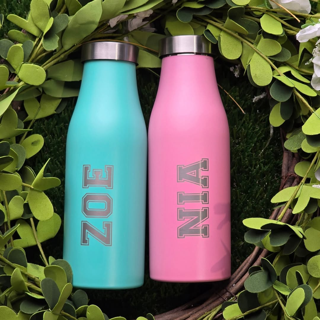 LAMOSE Robson 14 oz bottle in matte pink and teal, personalized with "NIA" and "ZOE" names, laid flat in a green wreath.