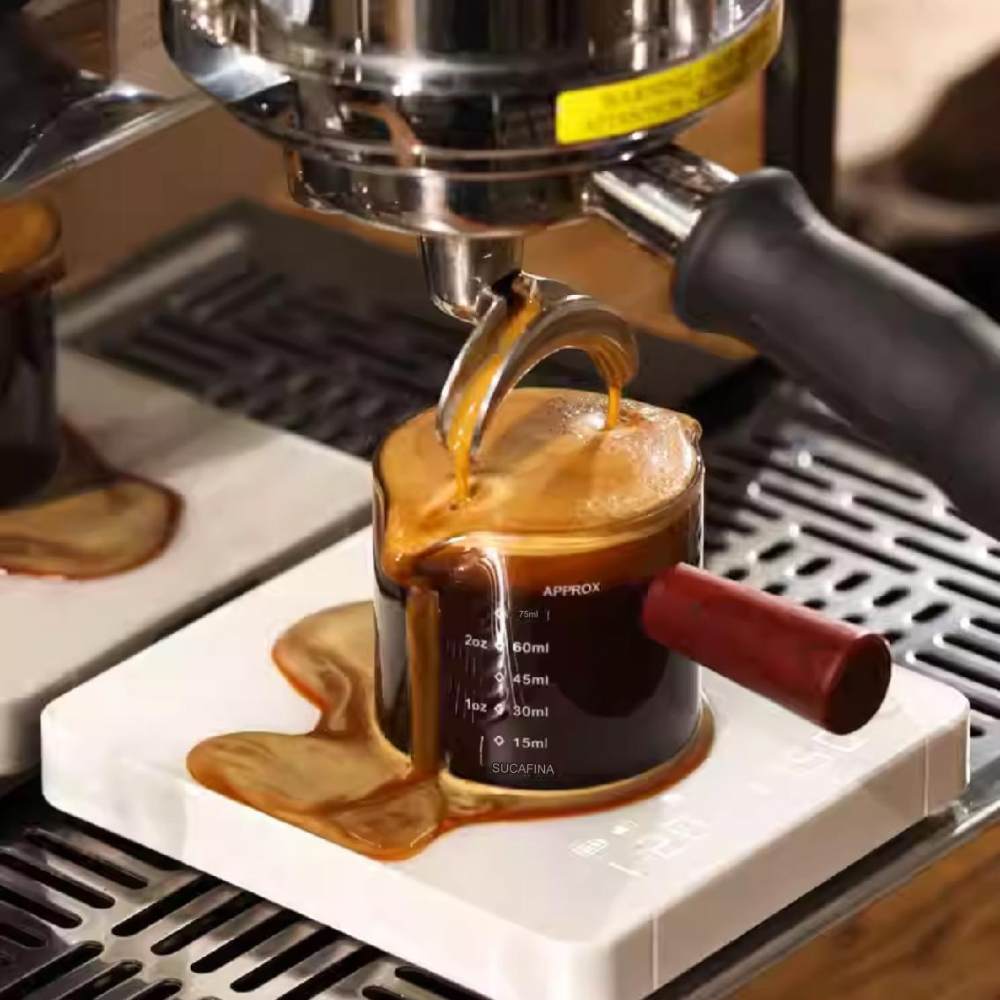 LAMOSE zeroHero Mini E-Smart Scale, a white digital coffee scale, measures an overflowing espresso shot from a glass cup during extraction.
