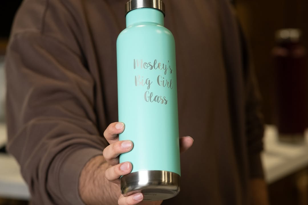 LAMOSE Moraine 27 oz mint stainless steel bottle held by a hand, front view, with 'Mosley's Big Girl Glass' engraving.